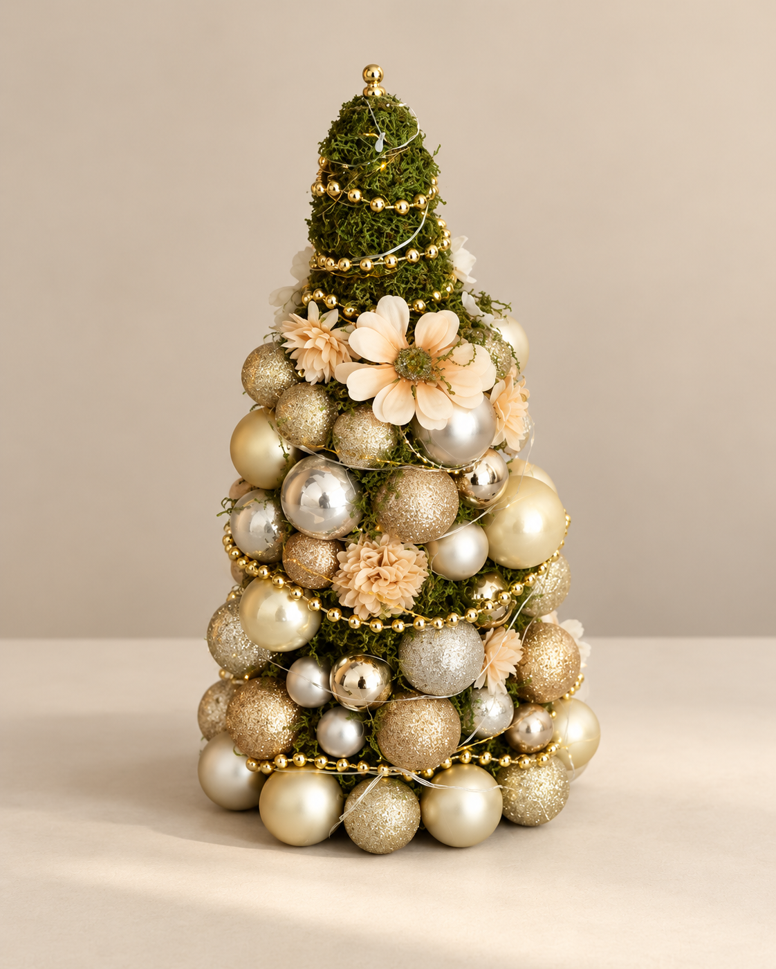 Kleine decoratieve kerstboom met crèmekleurige bloemen en champagnekleurige en zilveren kerstballen